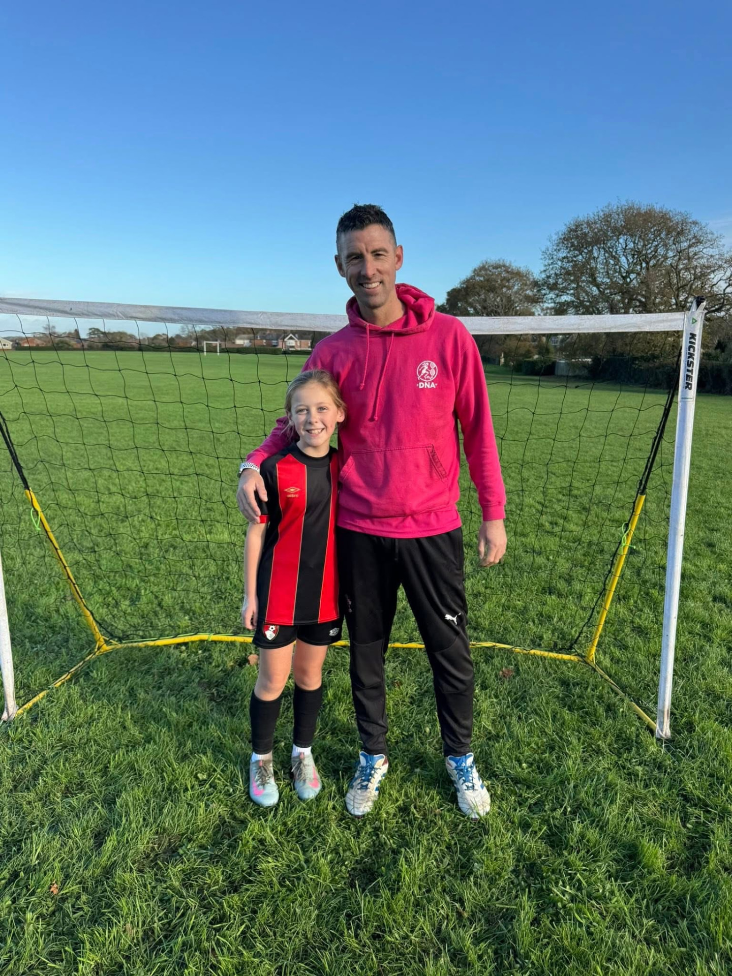 Dave Rimmer with a young player on a grass pitch in daylight