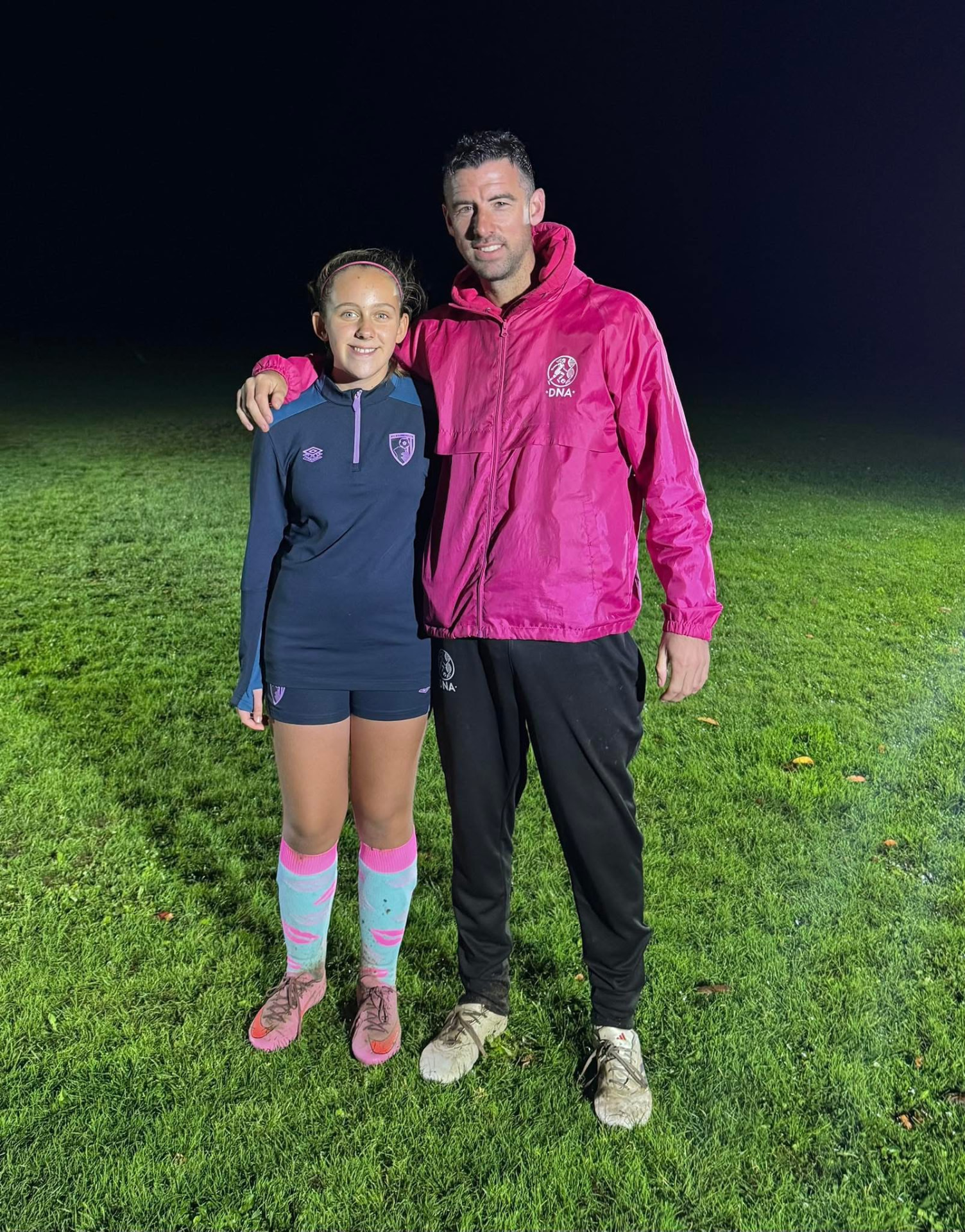 Dave Rimmer with a player on a floodlit pitch at night